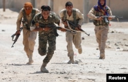 FILE - Kurdish fighters from the People's Protection Units (YPG) run across a street in Raqqa, Syria, July 3, 2017.