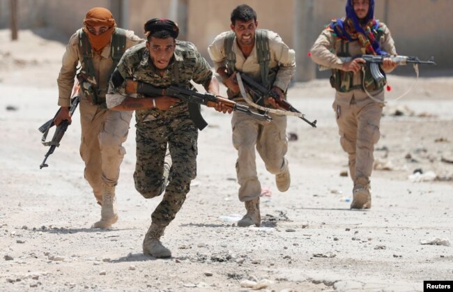 FILE - Kurdish fighters from the People's Protection Units (YPG) run across a street in Raqqa, Syria, July 3, 2017.