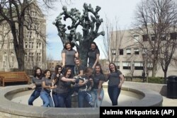 In this March 14, 2020 photo provided by Jaimie Kirkpatrick, Boston College seniors pop champagne beside the Tree of Life sculpture on the school's campus in Boston.