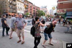 FILE - Steve Grillo, right, bumps elbows with a friend in the Hell's Kitchen neighborhood of New York, Friday, May 29, 2020, during the coronavirus pandemic. Grillo lives on the blocked-off street and is a walking advertisement touting his West Side commu