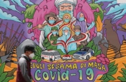 Seorang pria berjalan melewati mural bertema virus corona di Jakarta, Senin, 29 November 2021.