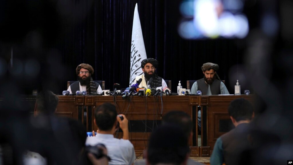 Frente a una bandera de los talibanes, el portavoz Zabihullah Mujahid, en el centro, habla en su primera conferencia de prensa, en Kabul, Afganistán, el martes 17 de agosto de 2021.