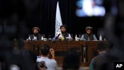 Frente a una bandera de los talibanes, el portavoz Zabihullah Mujahid, en el centro, habla en su primera conferencia de prensa, en Kabul, Afganistán, el martes 17 de agosto de 2021.