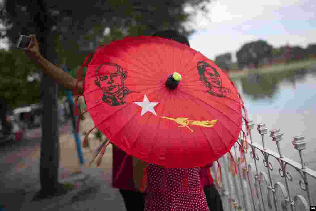 A group of people with an umbrella displaying pictures of Myanmar's opposition leader Aung San Suu Kyi, her late father General Aung San, and the logo of Suu Kyi’s National League for Democracy party take pictures of themselves in Mandalay. Myanmar’s general elections are scheduled for Nov. 8, 2015, the first since a nominally civilian government was installed in 2011.