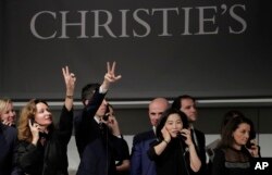 Bidding representatives motion for a bid on Armand Seguin's "Les delices de la vie" during an auction from the collection of Peggy and David Rockefeller, May 8, 2018, in New York.