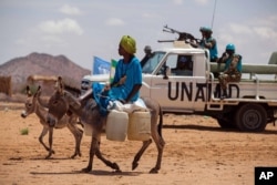 FILE - A man rides his donkey past Tanzanian UNAMID troops standing guard at a camp for internally displaced people in Khor Abeche, South Darfur, Sudan, June 30, 2014.