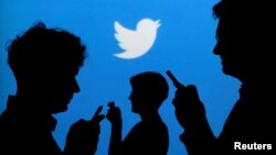 FILE - People holding mobile phones are silhouetted against a backdrop projected with the Twitter logo in this illustration.