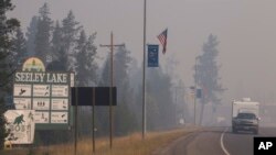 In this photo provided by the U.S. Forest Service a pickup pulls a camper through the wildfire smoke in Seeley Lake in Missoula County, Mont., Aug. 10, 2017. Health officials in western Montana are strongly recommending residents of Seeley Lake leave town because of hazardous smoke from area wildfires. 
