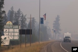 In this photo provided by the U.S. Forest Service, a pickup pulls a camper through the wildfire smoke in Seeley Lake in Missoula County, Mont., Aug. 10, 2017.