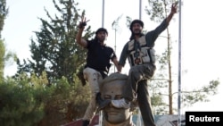 Members of the Free Syrian Army celebrate as they place their feet on a sculpture of late Syrian President Hafez al-Assad, father of Syrian President Bashar al-Assad, at the Brigade 52 military base in Daraa, Syria, June 9, 2015.