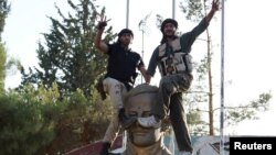 Members of the Free Syrian Army celebrate as they place their feet on a sculpture of late Syrian President Hafez al-Assad, father of Syrian President Bashar al-Assad, at the Brigade 52 military base in Daraa, Syria, June 9, 2015.