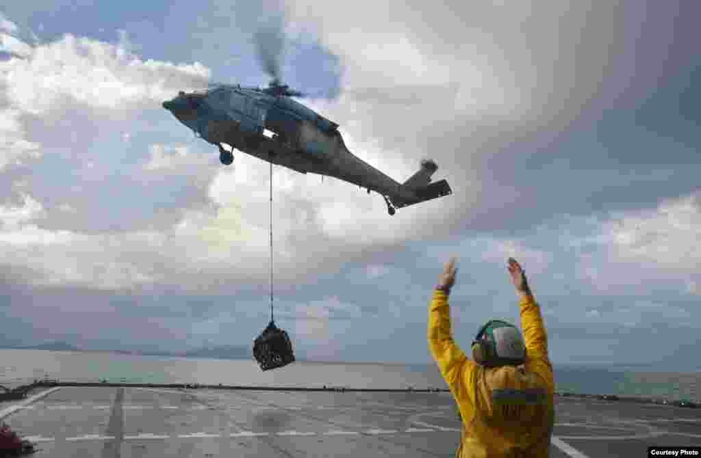 An Aviation Electrician’s Mate directs a MH-60S helicopter from the USNS Charles Drew as it lifts a pallet of diesel en route to the Philippines, Nov. 14. 2013. (U.S. Navy)