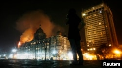 FILE - A reporter talks on her phone as smoke is seen coming from Taj Hotel in Mumbai, India, on Nov. 27, 2008, where terrorists were holding hostages during an attack that began the previous day.