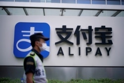 Seorang petugas keamanan melintas di depan logo pembayaran digital Alipay di Shanghai.