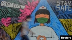 Seorang pejalan kaki berjalan dekat mural yang menggambarkan seorang perawat sebagai tanda dukungan kepada para medis yang menjadi garda terdepan penanganan wabah virus corona (COVID-19) di Ciamis, Jawa Barat, 10 April 2020. (Foto: Reuters)