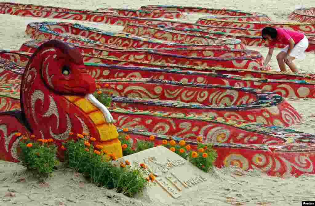 A volunteer prepares to pose for photos after the completion of a 100m (328 feet) long sand snake sculpture, entitled "Glittering Snake Trail" by Singaporean sand sculptor JOOheng Tan, during a media preview on Singapore's Sentosa Island.