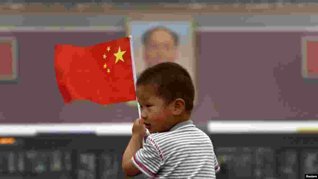 Seorang anak memegang bendera nasional China di depan potret mantan pemimpin Mao Zedong di Alun-Alun Tiananmen di Beijing (4/6) dalam peringatan 24 tahun pembantaian demonstran pro-demokrasi.