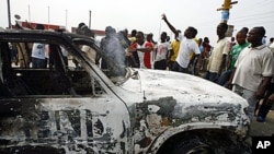 Ivorian students protest near a burnt U.N. vehicle during a demonstration at the junction of Riviera 2 in Abidjan, 13 Jan 2011