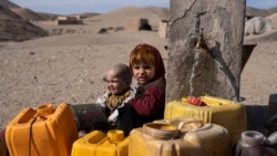 FILE - Two Afghan children sit next to a spigot as people of Kamar Kalagh village outside Herat, Afghanistan, try to fill their plastic containers with water, Nov. 26, 2021.
