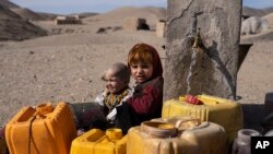 FILE - Two Afghan children sit next to a spigot as people of Kamar Kalagh village outside Herat, Afghanistan, try to fill their plastic containers with water, Nov. 26, 2021.
