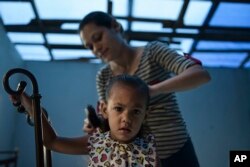 Wilmarie Gonzalez Rivera combs the hair of her daughter, Yeinelis Oliveras Gonzalez, 2, in Morovis, Puerto Rico, Dec. 22, 2017. The roof of their home was destroyed by Hurricane Maria; it's been replaced by a blue tarp and some recycled zinc pieces.