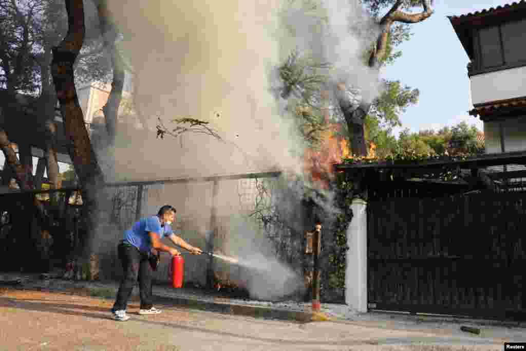 A man uses a fire extinguisher in an attempt to help fight a wildfire in Varympompi suburb north of Athens, Greece.