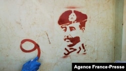 FILE - A person sprays graffiti next to a stencil painting of the Sudan's top army general, Abdel Fattah al-Burhan, with writing in Arabic that reads "leave," during a protest in Khartoum, Nov. 4, 2021, 
