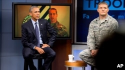 FILE - President Barack Obama, accompanied by Tech Sgt. Nathan Parry, takes a question from a service member in Afghanistan, on screen at center, during a town hall with service members at Fort Meade, Md., Sept. 11, 2015.