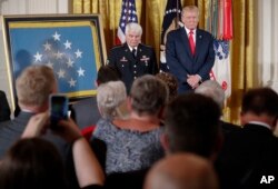 President Donald Trump stands on stage before bestowing the nation's highest military honor, the Medal of Honor, to retired Army medic Jim McCloughan, left, during a ceremony in the East Room of the White House in Washington, July 31, 2017.