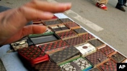 A vendor tries to prevent photographs being taken of fake Louis Vuitton and Coach brand purses she was selling on a street in Beijing.
