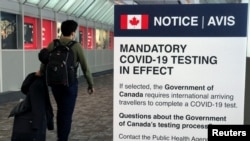 Seorang pelancong berjalan melewati papan pengumuman yang memberitahukan kewajiban untuk menjalani tes COVID-19 yang terpasang di Bandara Internasional Pearson, Toronto, Ontario, Kanada, pada 18 Desember 2021. (Foto: Reuters/Carlo Allegri)