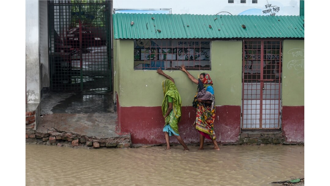 Warga berjalan di dekat rumah yang di sekelilingnya digenangi banjir menjelang topan Amphan, di Dacope, Distrik Khulna, 20 Mei 2020.