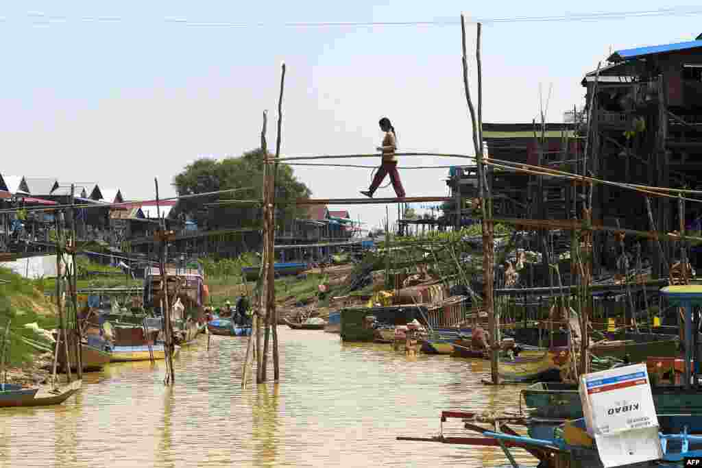 Kamboçya&#39;da bir kadın, Kampong Phluk kanalındaki bambu köprüden geçiyor.