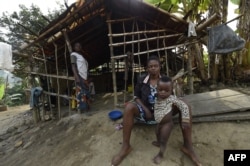 FILE - A Cameroonian refugee sit holding her child in front of a make-shift home, where hundreds are being sheltered, at Bashu-Okpambe village in Boki district of Cross Rivers State in southeast Nigeria, Jan 31, 2018.