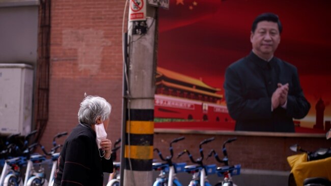 一名戴着口罩的妇女从上海街头一幅习近平的画像前走过。(2020年3月12日)