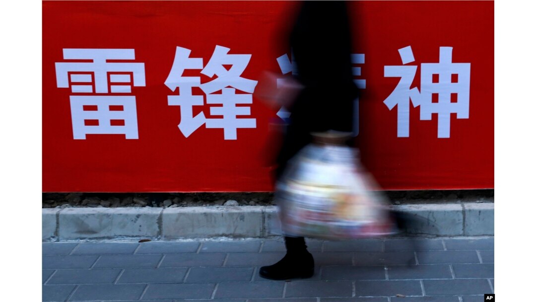 北京街头,一位女士路过宣传雷锋精神的广告标语(2019年3月5日)