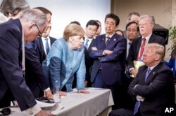 In this photo made available by the German Federal Government, German Chancellor Angela Merkel, center, speaks with U.S. President Donald Trump, seated at right, during the G7 Leaders Summit in La Malbaie, Quebec, Canada, on June 9, 2018.