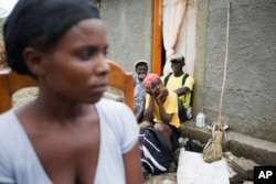 Neighbors sit on a stoop and listen as Bernadette Desravine (L) talks to a reporter about her missing father, Edma Desravine, who was last seen seeking refuge from the heavy rainfall and winds brought by Hurricane Matthew, in Port-a-Piment, a district of Les Cayes, Haiti, Oct. 18, 2016.