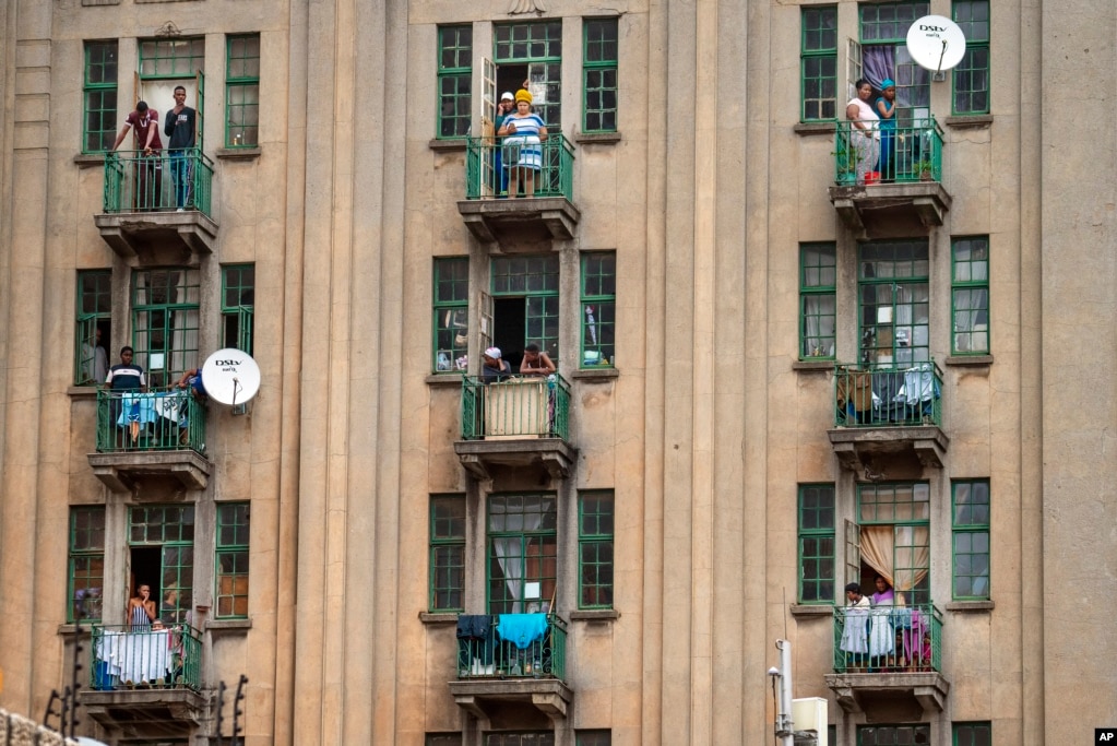 Residentes de un barrio del centro de&nbsp;Johannesburgo observan desde sus balcones que la policía sudafricana y las Fuerzas de Defensa Nacional buscan un bar local que creían que estaba abierto ilegalmente, a pesar de la cuarentena.&nbsp;