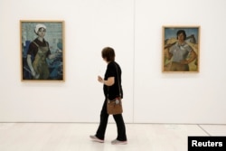 A visitor walks past the paintings "The Turner," left, by Albanian artist Zef Shoshi and "The Action Worker" by Hasan Nallbani during the documenta 14 art exhibition in the National Museum of Contemporary Art in Athens, Greece, May 9, 2017.