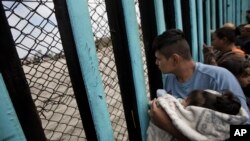 Seorang pria migran yang berusaha masuk ke Amerika, dengan meggendong putrinya, mengintip dari perbatasan Meksiko-AS (foto: ilustrasi). 