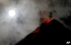 The super blue blood moon sets before dawn as lava cascades down the slopes of Mount Mayon volcano during a mild eruption as seen from Sto. Domingo township, Albay province around 340 kilometers (200 miles) southeast of Manila, Philippines, Feb. 1, 2018.