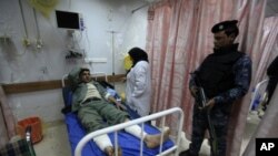 一位在2月19日伊拉克警校爆炸案中受伤的人在巴格达一所医院接受治疗，他的同伴站在床前警戒