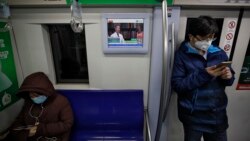 Masked commuters ride in a subway train as a monitor showing a doctor talks about precaution of COVID-19 virus, in Beijing, Monday, Feb. 17, 2020. (AP Photo/Andy Wong)