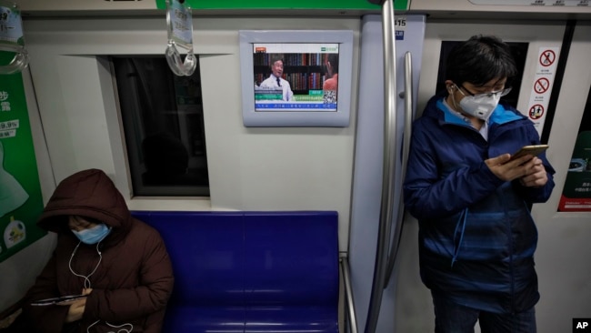 Masked commuters ride in a subway train as a monitor showing a doctor talks about precaution of COVID-19 virus, in Beijing, Monday, Feb. 17, 2020. (AP Photo/Andy Wong)