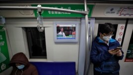 Masked commuters ride in a subway train as a monitor showing a doctor talks about precaution of COVID-19 virus, in Beijing, Monday, Feb. 17, 2020. (AP Photo/Andy Wong)
