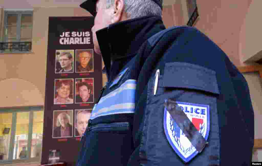 A French municipal police officer, whose badge patch is barred in black for mourning, stands by a poster showing victims of the shooting at the Paris offices of Charlie Hebdo in Nice, Jan. 8, 2015. 