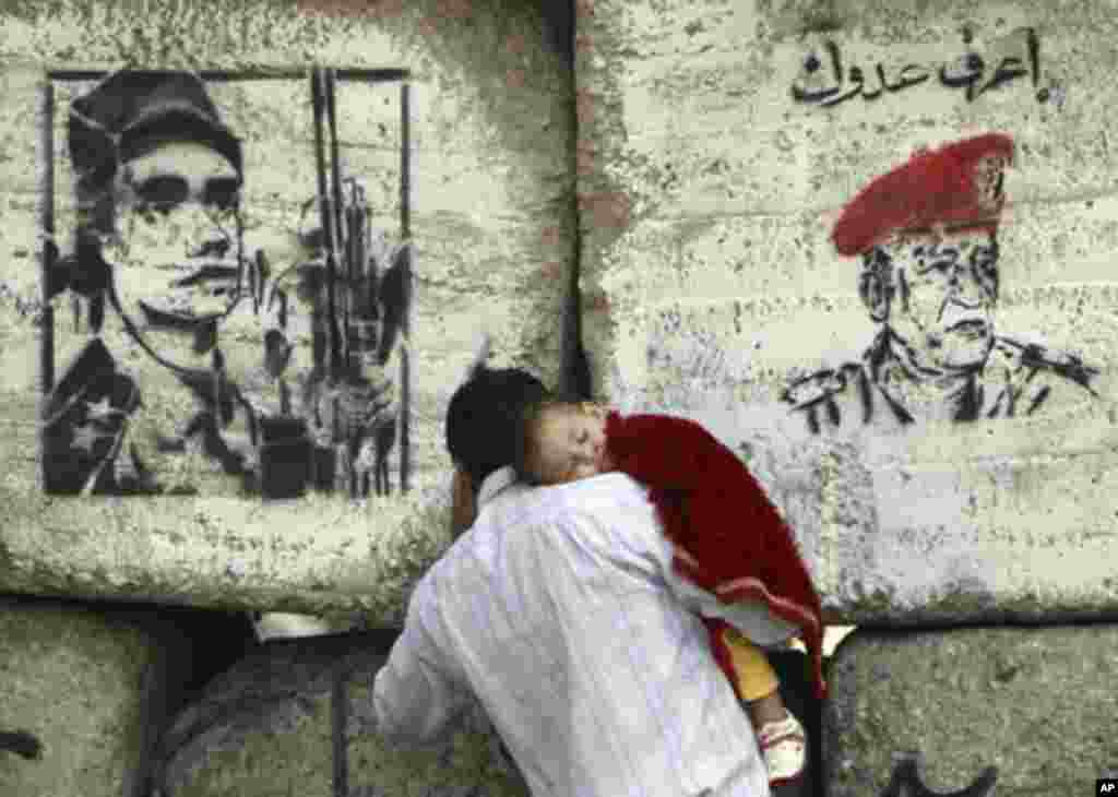 A man carries his child in front of barricades built by the Egyptian military at Mohamed Mahmoud street which leads to the Interior Ministry, where clashes between protesters and security force took place in late November, near Tahrir Square in Cairo Dece