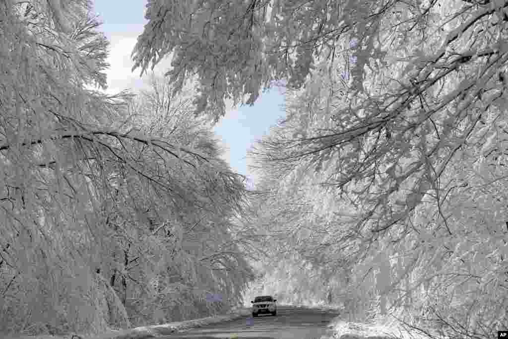 A car makes its way through a snowy landscape in Highland Falls, New Jersey.