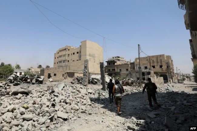 FILE - Fighters from the Syrian Democratic Forces (SDF), a U.S.-backed Kurdish-Arab alliance, walk through the rubble in an eastern area of the embattled city of Raqqa in northern Syria, Aug. 15, 2017.